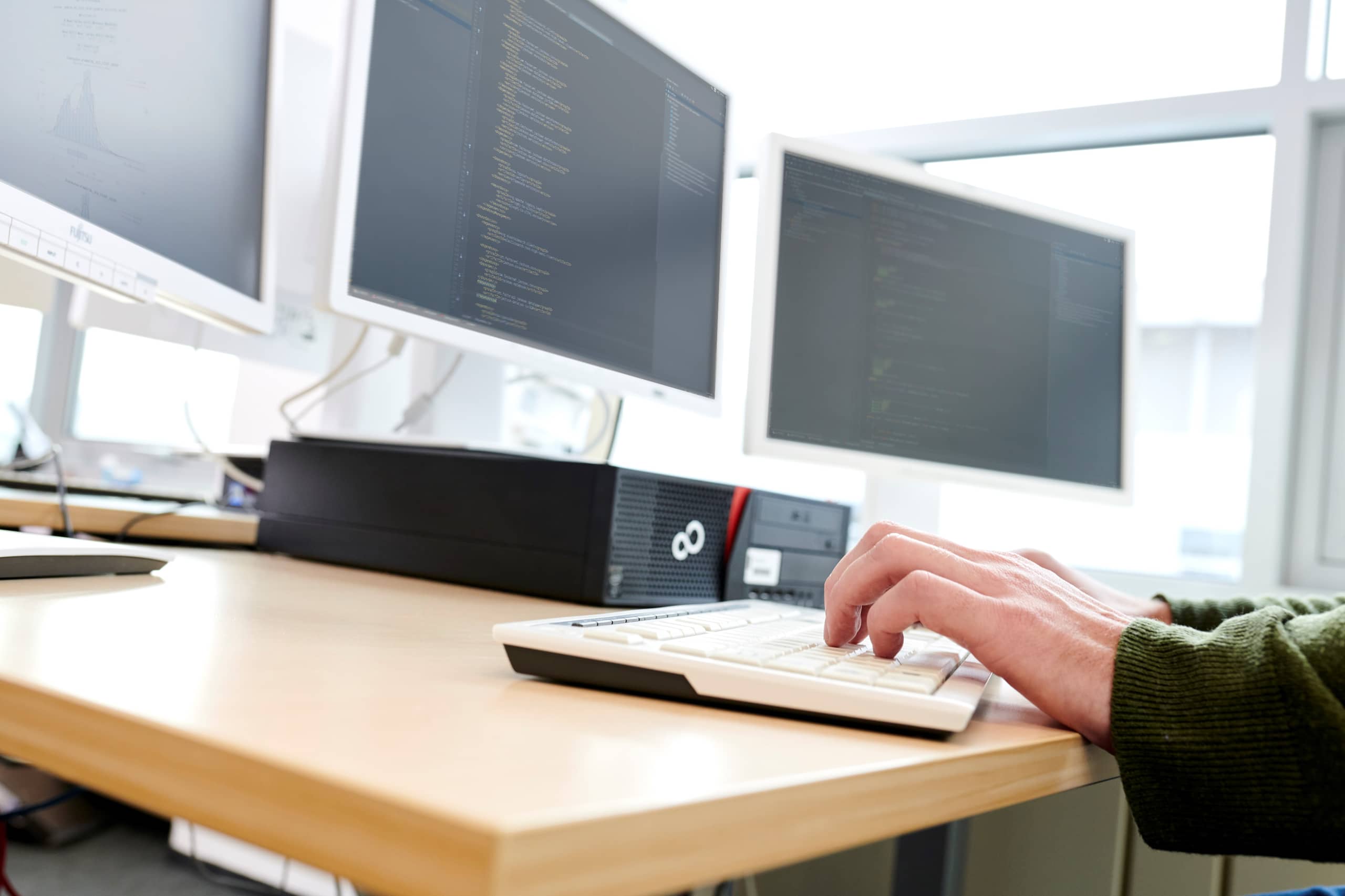 Close-up van drie computerschermen en een hand op een toetsenbord