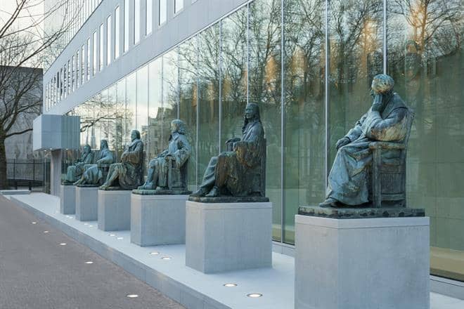 Een rij beelden naast een glazen wand van een gebouw
