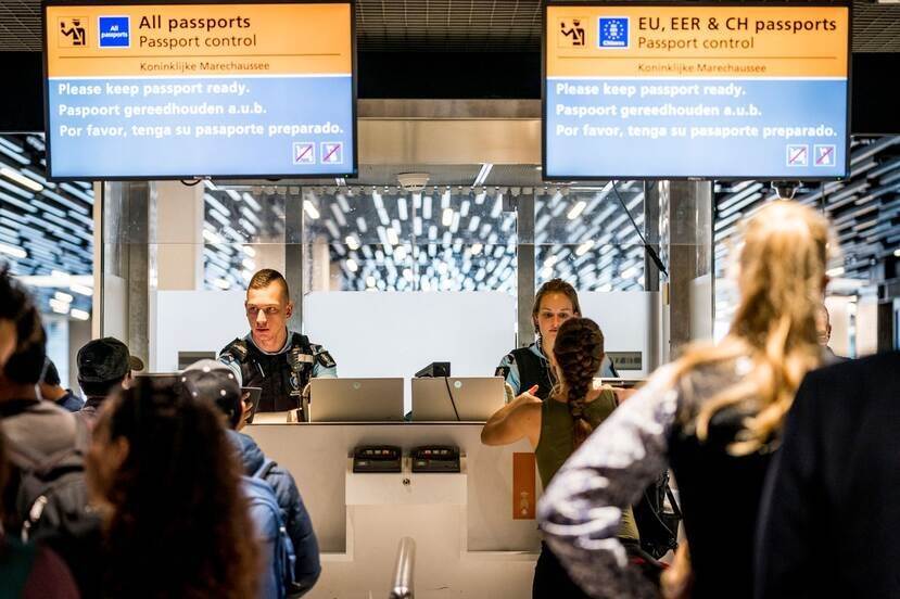 Paspoortcontrole op Schiphol met reizigers en marechaussee